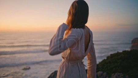 Flexible girl dancer moving hands performing dance on evening sea coast back view. Performer dancing choreography looking sundown on grassy hills closeup. Woman body improvising contemporary style 