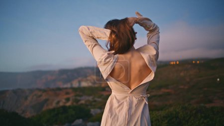 Romantic lady dancing sunset nature making relaxed movements on ocean cliff. Young girl wearing dress with naked back moving sensually on green grass hill. Graceful woman enjoy passionate dance alone 