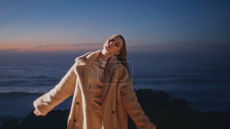 Relaxed girl contemporary dancer waving hair performing on ocean beach summer evening. Party chill woman wearing fur coat dancing modern style enjoying on sand seashore. Festive lifestyle concept