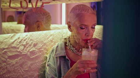 Stilvolle Senioren trinken Cocktail entspannen in Abendcafé Nahaufnahme. Coole reife Frau ruht sich allein aus und nippt an einem alkoholischen Getränk im Club. Herrliche graue Haare Modell suchen Kamera genießen Nachtleben am Wochenende.