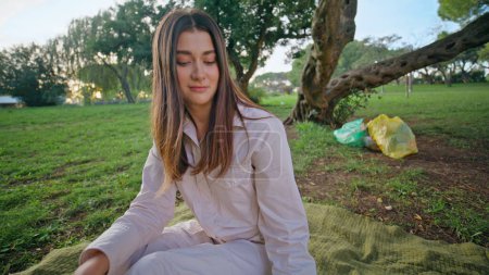 Serene woman relaxing picnic in park closeup. Beautiful girl sitting blanket drinking lemon water at green surroundings. Volunteer enjoy leisure activity in tranquil environment after nature cleanup