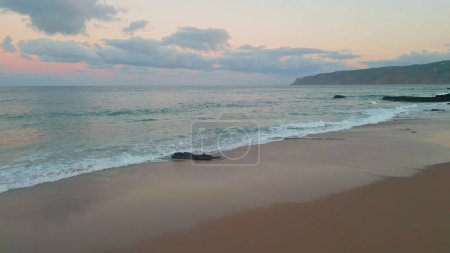 Tranquil ocean landscape aerial view. Twilight painting horizon with pink shades. Gentle waves lap against serene beach as sun set. Peaceful evening coastline drone shot. Pastel panoramic seashore.