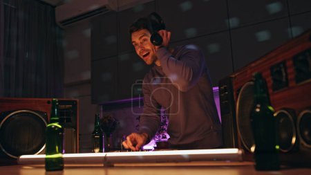 Professionelle DJ-Mixing-Tracks mit modernem Equipment auf der Bühne Nachtdisco Club aus nächster Nähe. Fröhlicher Discjockey-Sound in drahtlosen Kopfhörern. Lächelnder Mann erstellt Remixe auf Audio-Konsole.