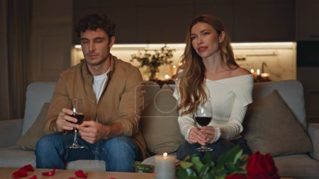 Shying couple having date in cozy evening apartment. Cute pair spending evening together sitting home couch with wine glasses. Two people talking trying to flirt in romantic candles atmosphere.