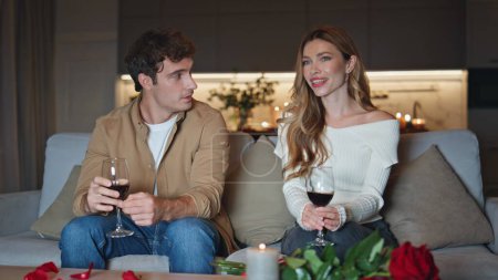 Pair talking at romantic date on home couch close up. Two shying people sitting apartment sofa with wine glasses enjoying evening candles atmosphere. Young couple have friendly conversation indoors.
