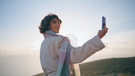 Reisefrau fotografiert schöne Naturansichten in Smartphone-Nahaufnahme. Lächelnde Dame, die den wunderschönen Sonnenuntergang mit ihrem Handy fotografiert. Reiseleiterin fängt malerische Landschaft ein, die Glück ausstrahlt.