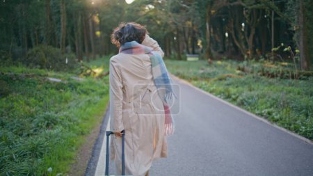 Belle promenade pédestre sentier forestier avec valise incarnant le voyage. Femme chic en écharpe flânant route en bois à matin tranquille incarnant la luxure de l'errance. Explorateur à la mode profiter du voyage de vacances.