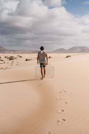Photo for Young man walking calmly on the desert sand of the dunes of Corralejo in Fuerteventura, in summer, during a vacation trip through the Canary Islands - Royalty Free Image