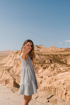 Foto de Chica con vestido y gafas de sol de pie y mirando a la cámara en el desierto de las Bardenas Reales de Navarra en verano - Imagen libre de derechos