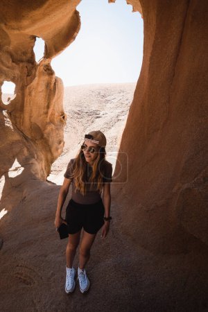 Téléchargez les photos : Fille heureuse explorant les formations rocheuses d'un canyon désertique à Fuerteventura pendant ses vacances - en image libre de droit