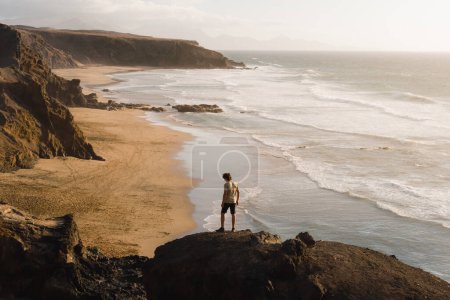Téléchargez les photos : Jeune homme profite du coucher de soleil sur la côte de Fuerteventura tout en visitant les îles Canaries - en image libre de droit