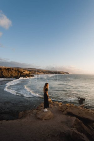 Foto de Mujer joven disfruta de la puesta de sol en la costa de Fuerteventura mientras visita las Islas Canarias - Imagen libre de derechos