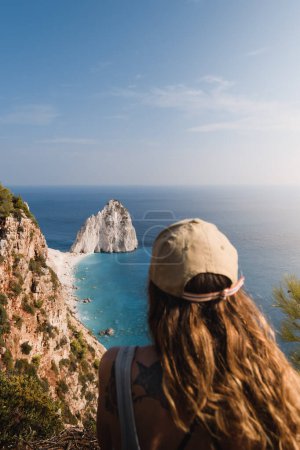 Téléchargez les photos : Jeune femme en bonnet de soleil regardant les spectaculaires falaises blanches et les eaux turquoise de l'île grecque de Zakhyntos pendant son voyage touristique d'été aux îles Ioniennes - en image libre de droit