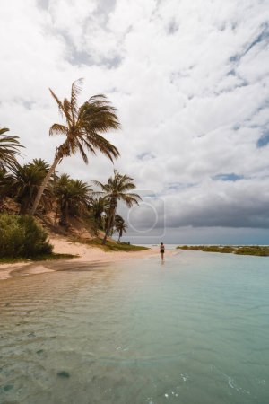 hermosa playa tropical con agua turquesa, cielo azul y palmeras en la isla canaria turística de fuerteventura. Con una mujer caminando a través de ella en medio