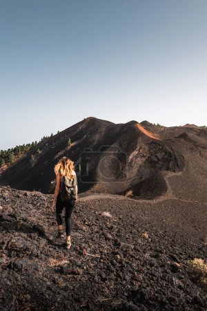 Foto de Mujer entre lava haciendo trekking al atardecer a través de las montañas de roca volcánica de Cumbre Vieja en la isla canaria de La Palma - Imagen libre de derechos
