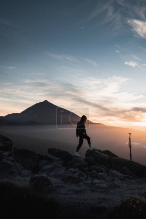 Téléchargez les photos : Jeune femme en tenue urbaine jouissant entre les rochers de la montagne au coucher du soleil avec le volcan Teide en arrière-plan. Au cours de son voyage de vacances sur l'île Canaries de Ténérife - en image libre de droit