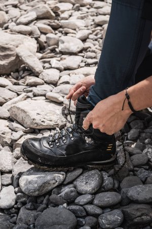 Téléchargez les photos : Homme attachant ses bottes de randonnée sur des pierres lors d'une aventure de trekking - en image libre de droit