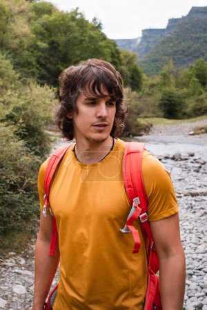 Foto de Chico joven con pelo largo y mochila trekking en el bosque, en un ambiente verde de verano o primavera - Imagen libre de derechos