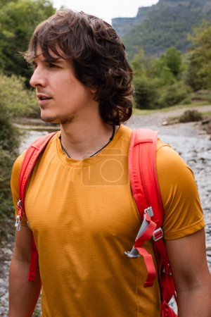 Photo for Young man with long hair and backpack in the mountains, in a green environment in summer - Royalty Free Image
