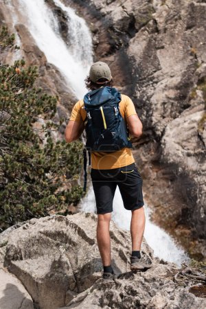 Junger Mann mit Rucksack beobachtet einen Wasserfall in Panticosa während seiner abenteuerlichen Wanderung durch die Pyrenäen