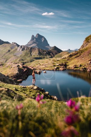 Téléchargez les photos : Beau paysage des ibones ou des lacs d'anayet avec le pic Midi d'Ossau en arrière-plan et des fleurs roses au premier plan et une fille profitant des Pyrénées - en image libre de droit
