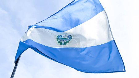 Téléchargez les photos : Vue à angle bas du drapeau national El Savador agitant dans le vent sous un ciel bleu nuageux. Concept de patriotisme et de nationalisme - en image libre de droit