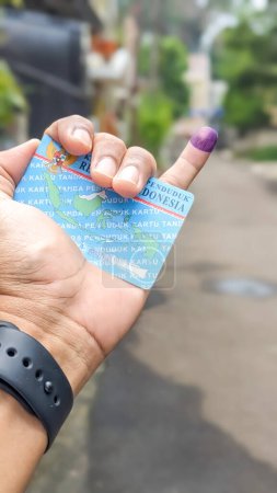 Vista de cerca de una mano sosteniendo un documento de identidad indonesio con tinta púrpura aplicada en el dedo meñique después de las elecciones presidenciales en Indonesia. Concepto del partido Democracia