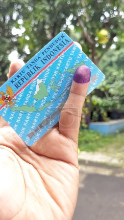 Vista de cerca de una mano sosteniendo un documento de identidad indonesio con tinta púrpura aplicada en el dedo meñique después de las elecciones presidenciales en Indonesia. Concepto del partido Democracia