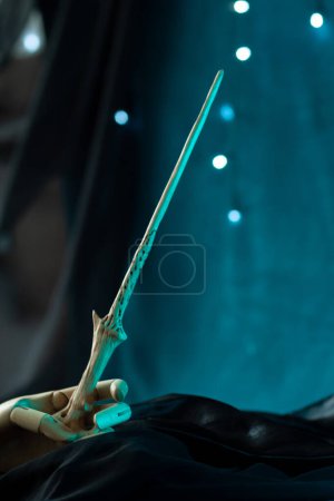 Photo for The sorcerers magical artifact is held by a wooden hand. Magic wand on dark background with shining lights, drenched in green neon light, close-up, vertical - Royalty Free Image