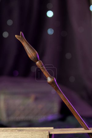 Photo for The magic wand is made of wood, decorated with figured carvings and a limb carved in the shape of a flower bud. The magical artifact stands on a purple background with shining bokeh, vertically - Royalty Free Image