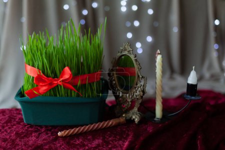 Tarjeta de felicitación para vacaciones Nevruz, año nuevo iraní. Símbolos tradicionales de germen de trigo, espejo, vela sobre fondo rojo con luces brillantes, primer plano