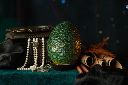 A large green scaly dragon egg stands on a stand next to an antique chest with a necklace among scrolls and fabrics, on a dark background with glowing bokeh. Fabulous treasures, close-up