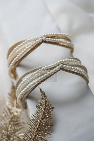Two golden hair hoops are adorned with necklaces on a white stand next to shiny leaves. Accessories decoration for hairstyle, close-up vertically