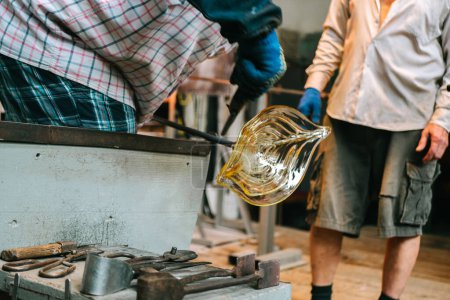 Die Hände des Dachrinnenmeisters formen in der Werkstatt zwischen den Werkzeugen ein geschmolzenes Glasprodukt. Der Prozess der Herstellung einer gläsernen Figur, Nahaufnahme