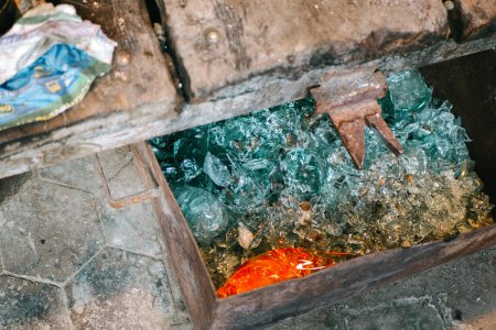 A metal box filled with pieces of glass of various shapes. hardness, the temperature that is cut off, is discarded after blowing. Glass production workshop, close-up