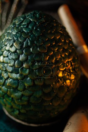 Green shiny golden scales of decorative dragon egg on dark background with blue bokeh. Props for fabulous halloween costume, close-up texture vertically
