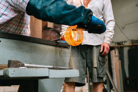 Die Hände des Dachrinnenmeisters formen in der Werkstatt zwischen den Werkzeugen ein geschmolzenes Glasprodukt. Der Prozess der Herstellung einer gläsernen Figur, Nahaufnahme