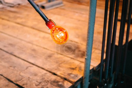 Eine Kugel aus heißem geschmolzenem Glas wird am Ende eines Eisenrohres vor dem Hintergrund eines Holzfußbodens in einer Werkstatt geblasen. Der Prozess der Herstellung eines Produkts in einer Glasfabrik, Nahaufnahme
