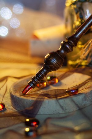 Wooden chiseled figured decorative handle of a magic stick with a crystal on top among round glass stones against a background of shining lights under golden light. Close-up, vertical