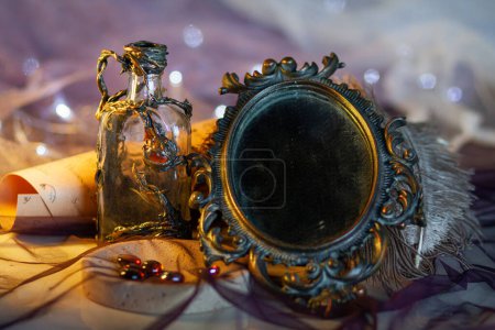Glass decorative bottle decorated with three dimensional ornament among vintage magic objects on a shining purple background with golden light. Fabulous props, close-up 