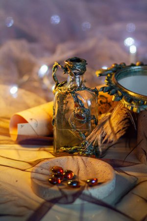 Glass decorative bottle decorated with three dimensional ornament among vintage magic objects on a shining purple background with golden light. Fabulous props, close-up vertical