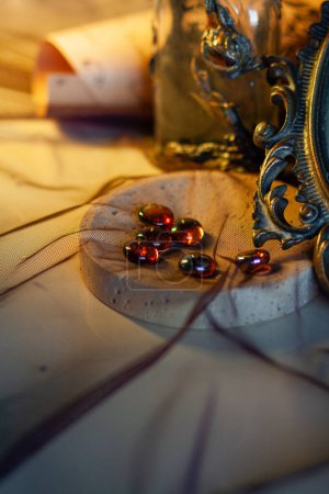 Glowing glass round stones lie in a heap in a decorative bowl next to an old vintage mirror with a curly metal frame against a warm golden light. Close-up, details vertically