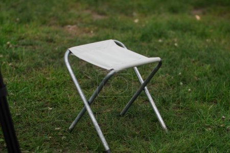 Una silla plegable de camping y picnic con un marco de metal y un asiento de tela ligera se sienta en la hierba. Muebles turísticos verticalmente primer plano