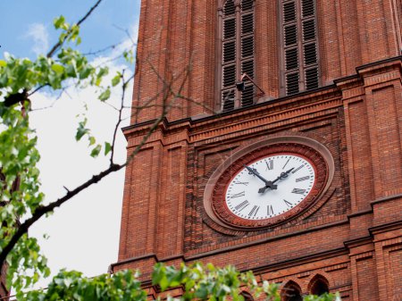 Photo for Church clock with white clock face. Close up red brick church tower with clock. Ancient clock with old white and black clock-face. Sunny day with blue sky and few clouds. - Royalty Free Image