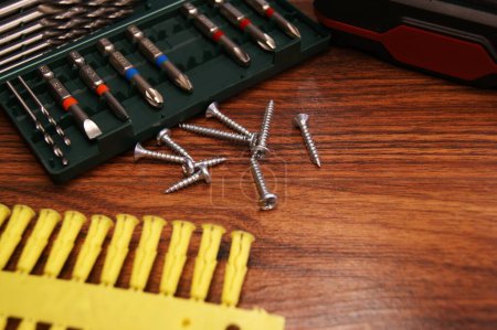 A set of bits and mounting screws on a dark wooden table.