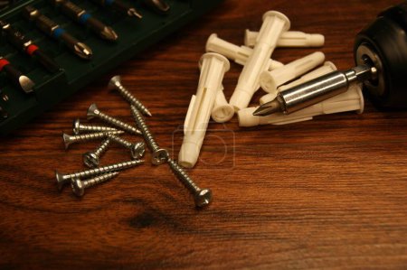 Dowels, screws, screwdriver, bit set. Tools and fasteners on a wooden surface