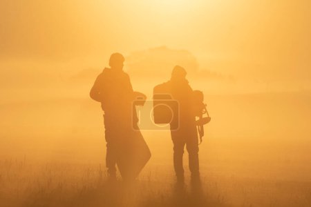 Photo for Silhouettes of a man and a woman in a military suits with a backpacks on the background of the sunset - Royalty Free Image