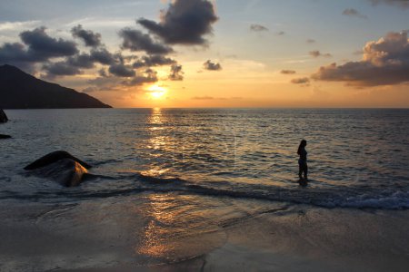 Téléchargez les photos : Seychelles, 26 février 2015 - Un amateur de plage profite d'un moment tranquille dans le contexte d'un coucher de soleil tropical glorieux sur la plage de Beau Vallon - en image libre de droit
