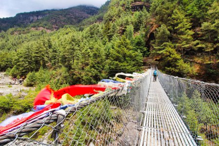 Photo for Trekkers on the Everest Base Camp trek pass over steel rope bridges over streams adorned with prayer flags near Namche Bazaar,Nepal - Royalty Free Image