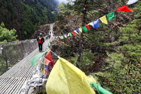 Photo for Trekkers on the Everest Base Camp trek pass over steel rope bridges over streams adorned with prayer flags near Namche Bazaar,Nepal - Royalty Free Image